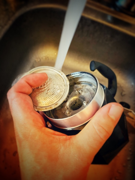 Ein auseinandergeschraubter Mokka Pot bei der Reinigung unter fließendem Wasser. Das ist ein wichtiger Teil um immer leckeren Kaffee machen zu können.