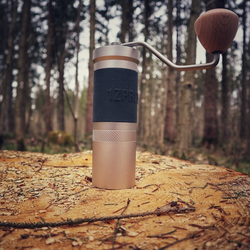 Die manuelle Kaffeemühle 1Zpresso JX Pro steht auf einem Holzstamm im Wald.