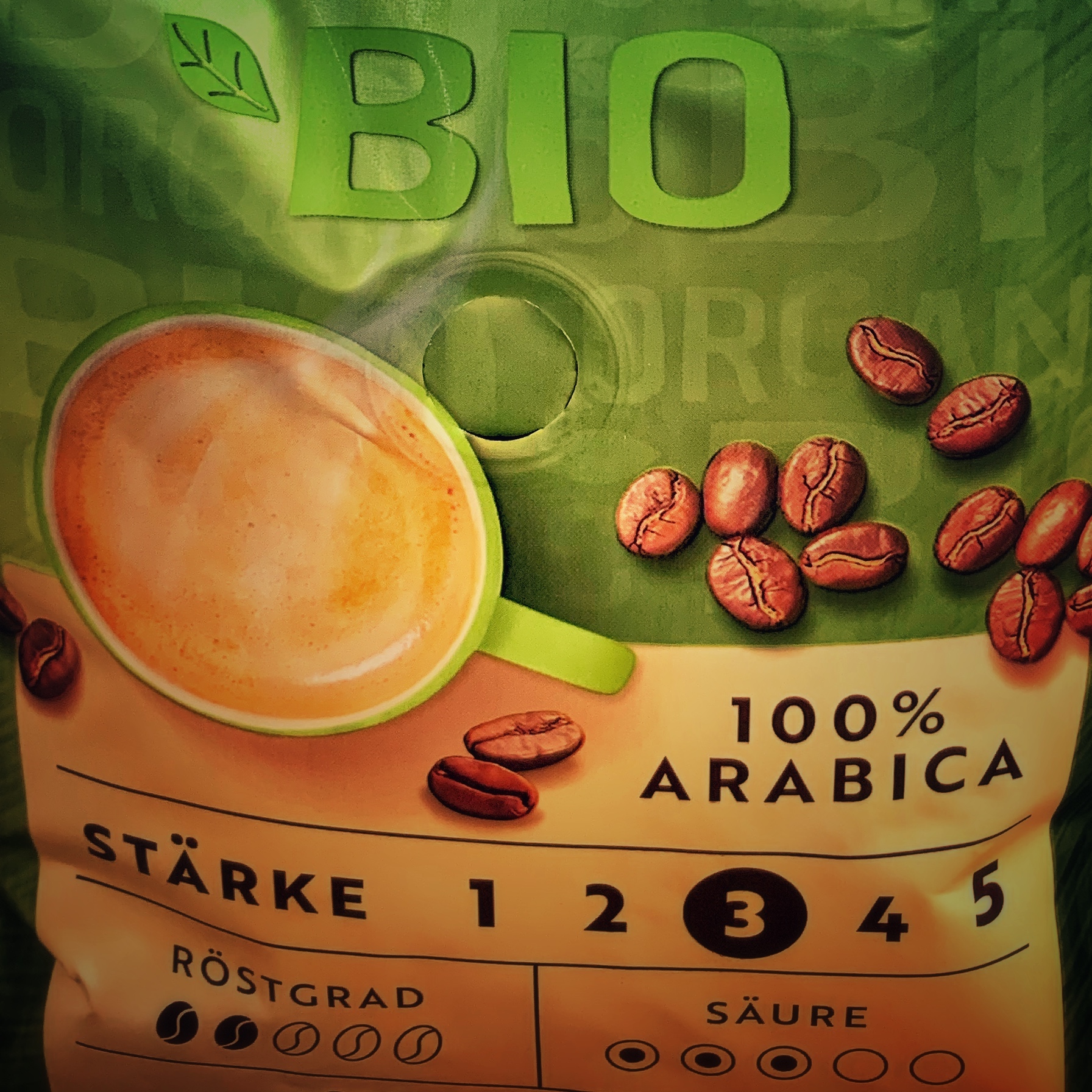 Eine grün braune Kaffeepackung mit der typischen Stärkeangabe in Nahaufnahme. Es steht geschrieben: 100% Arabica, der Röstgrad 2, die Säure 3 und die Stärke 3. Aber gibt es starke Kaffeebohnen?