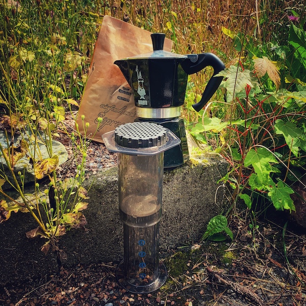 Eine Bialetti, eine AeroPress und eine Tüte Kaffee in hohem Gras. Wie macht man Kaffee richtig?