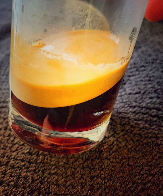 Kaffee und Crema in einem Longdrink Glas, in der Nahaufnahme vor einem schwarzen Handtuch.