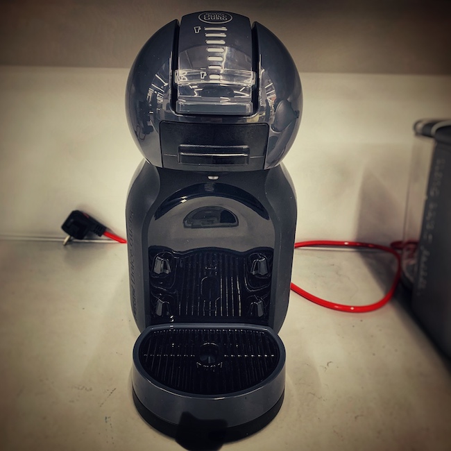 Eine Kapsel Kaffee Maschine in all ihrer grauen Pracht in einem grauen Regal.