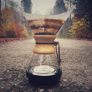 Eine Chemex Filterkaffee Karaffe auf einem Weg im herbstlichen Wald mit frisch gebrühtem Kaffee darin.
