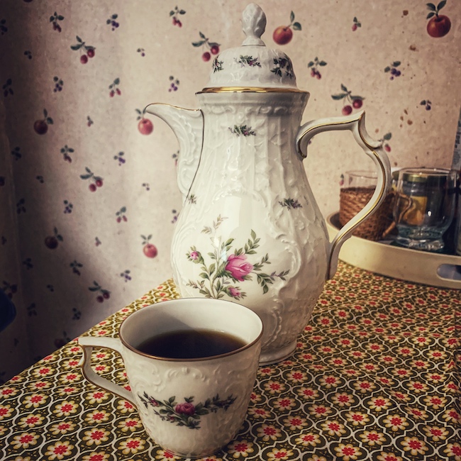 Klassische Blümchen Kaffeekanne für den Filterkaffee beim Kaffeekränzchen., steht auf einem Tisch, gemeinsam mit einer Tasse gefüllt mit schwarzem Kaffee, in einer Küche.