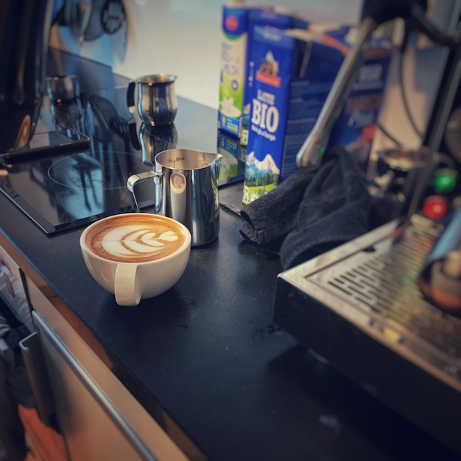 Eine Station zum Milchschaum machen neben einer Espressomaschine. Man sieht gegossene Latte Art in einer Tasse.
