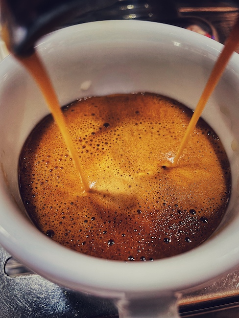 Espresso läuft in eine Tasse. Verwendet wurde zu frischer Kaffee, was man an den vielen Blasen sieht.